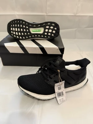 Svarta Adidas Ultraboost sneakers - Svarta Adidas Ultraboost sneakers med stickad ovandel, vita Boost-sulor och svarta detaljer. Klassisk låg modell med svart yttersula och snörning. Perfekta för dig som gillar stilrena och bekväma skor.
