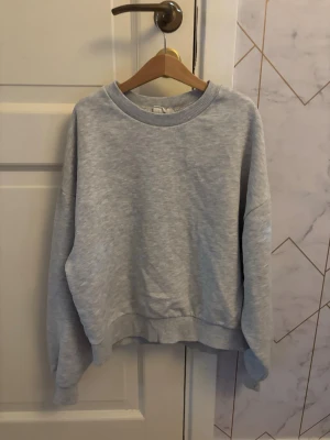 Ljusgrå sweatshirt utan huva - En basic ljusgrå sweatshirt i mjukt material med rund halsringning och ribbade muddar vid ärmslut och nederkant. Perfekt för en avslappnad och enkel stil. Passar till det mesta och är superbekväm.