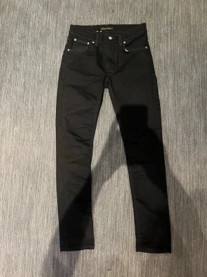 Svarta jeans från Nudie  - Säljer ett par klassiska svarta jeans från Nudie Jeans. De har perfekt passform och mkt sköna. Detta är ett ryktigt schysst par, med riktigt fet tvätt. De är i storlek 30/32 (W30 & L32). De passar väldigt bra till nästan allt, vilket gör dem väldigt lätt att matcha. Jag skulle säga att 269kr är ett väldigt bra pris för ett par i detta skick och utseende! Nypris: 1800 typ & skick: 10/10 (precis nya). Hör bara av dig vid minsta fundering & priset är inte hugget i sten!