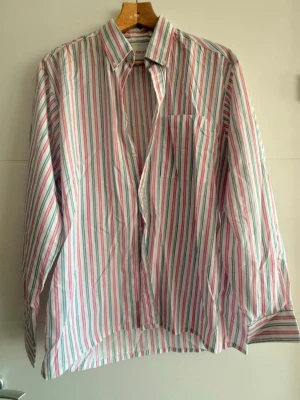 ✨👔 Snygg herrskjorta med färgglada ränder 🌈🔥 - ✨👔 Snygg herrskjorta med färgglada ränder 🌈🔥  ✔️ Storlek: 40 📏 ✔️ Bredd: 120 cm 📐 ✔️ Längd: 70 cm 📏 ✔️ Material: 65% polyester 🧵 / 35% bomull 🌿  Mycket bra skick 💯👌 Perfekt för både vardag 🏙️ och fest 🎉✨  💬 Hör gärna av dig! 📩 🛍️ Välkommen att köpa! 