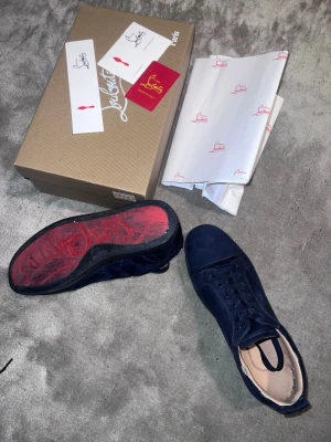Marinblå sneakers från Louboutin - Snygga marinblå sneakers från Christian Louboutin i mocka med klassisk röd sula och broderad logga på hälen. Skorna har lågt skaft, rund tå och matchande marinblå snörning. Perfekta för dig som vill sticka ut med exklusiv design och lyxiga material. Pris kan diskuteras med tanke på att de är använda👍