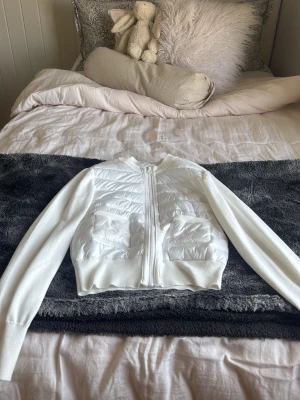 Vit quiltad cardiganjacka GINA TRICOT BARN - Snygg vit cardiganjacka med quiltad framsida och två praktiska fickor. Jackan har ribbade muddar, dragkedja framtill och stickade ärmar. Perfekt för lager på lager och ger en clean look till din outfit.