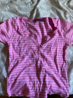 Rosa randig topp med knappar - Säljer en rosa och ljusrosa randig topp från Brandy Melville. Brukt 2-3 ganger