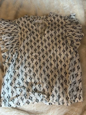 Vit blus med svart mönster och volang - Snygg blus med mönster, som är ny utan prislapp. Från Zalando 
