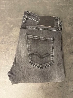 Grå slim fit jeans från Replay, 33/34 - Snygga grå slim fit jeans från Replay med klassisk femficksmodell och diskret slitning. Jeansen har en mörkgrå tvätt, raka ben och detaljerade sömmar på bakfickan. Perfekta för en trendig och avslappnad stil.