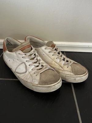 Vita sneakers från Philippe Model - Snygga vita sneakers från Philippe Model med beige detaljer och bruna partier vid hälen. Skorna har klassisk låg profil, vita snören och är tillverkade i läder och mocka. Perfekta för en avslappnad och trendig stil. 100% äkta, finns qr kod och pris kan diskuteras. Låda medföljer!