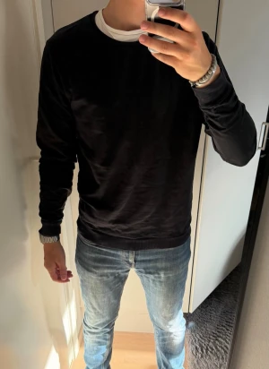 Svart sweatshirt med rund hals - En stilren svart sweatshirt med rund hals och långa ärmar. Tröjan har ribbade muddar vid ärmslut och nederkant. Perfekt basplagg som passar till det mesta och är enkel att matcha med jeans eller andra byxor.