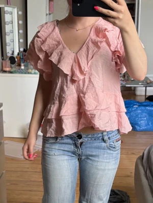 Ljusrosa volangblus med v-ringning - Söt ljusrosa blus med v-ringning och stora volangdetaljer framtill och på ärmarna. Blusen har en lös passform och är kortare i modellen, vilket ger en luftig och trendig look🧘🏼‍♀️💗