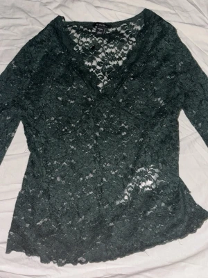 Mörkgrön spetsblus från Amisu - Snygg mörkgrön långärmad blus från Amisu i genombruten spets med v-ringning. Perfekt att styla lager på lager eller med ett linne under. Blusen har en feminin och elegant look med fina spetsdetaljer.
