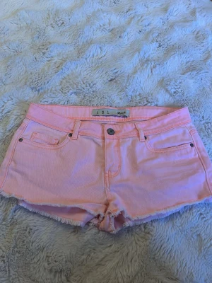 Ljusrosa shorts från Denim Co. - Säljer ett par ljusrosa shorts från Denim Co. i klassisk femficksmodell. Shortsen har råa kanter nedtill och knappgylf. Perfekta för varma dagar och har en snygg, enkel design som är lätt att matcha.