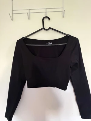 Svart croppad topp med lång ärm - Snygg svart croppad topp från Weekday med lång ärm och fyrkantig ringning. Tillverkad i ett stretchigt material som sitter tajt och bekvämt. Perfekt att styla med höga jeans eller kjol för en trendig look. Har aldrig använt helt nytt☺️