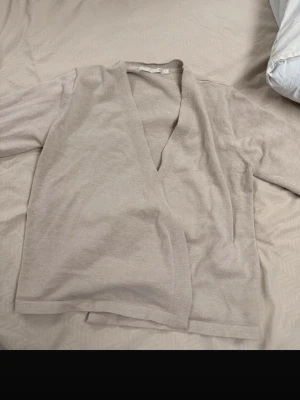 Beige öppen kofta i mjukt material - Säljer en stilren beige kofta med öppen front och lång ärm. Koftan är tillverkad i ett mjukt, tunt material och har en avslappnad passform. Perfekt att slänga över en topp för en enkel och clean look.