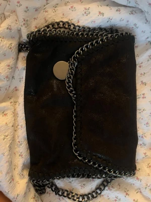 Jättefin väska - Snygg svart kuvertväska med grova silverfärgade kedjor längs kanterna och som axelrem. Väskan har ett stort runt metallspänne och insidan är fodrad med leopardmönster. Perfekt för dig som gillar en edgy och trendig stil.