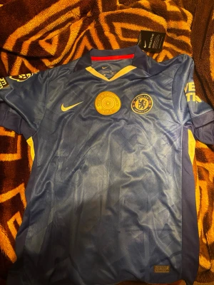 Chelsea matchtröja João Pedro #20 Nike - Snygg blå Chelsea matchtröja från Nike med João Pedro och nummer 20 på ryggen. Tröjan har officiella klubbmärken, Premier League-logga och World Champions FIFA-märke på bröstet. Korta ärmar och ventilerande material, perfekt för fotboll eller träning.