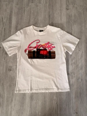 Vit t-shirt med tryck och text - Vit t-shirt med färgglatt tryck av en bomb med digital klocka och graffiti-liknande detaljer på framsidan. På baksidan står det 'NO TIME 4 LUV' i stora svarta bokstäver. Klassisk passform och rund hals.