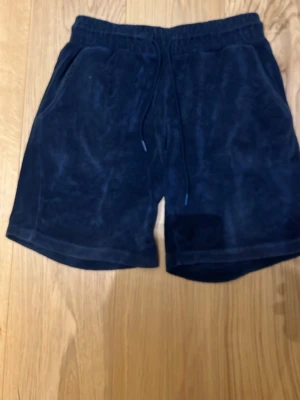 Mörkblå frottéshorts med snörning - Mörkblå shorts från Jack&Jones i mjuk frotté med elastisk midja och snörning. Två sidofickor fram och en bakficka med liten logotyp. Perfekta för sommardagar när du vill vara både chill och snygg. Det är XS men passar ochså S