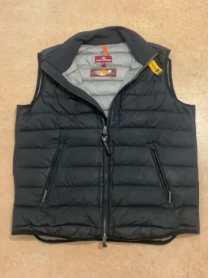 Svart dunväst från Parajumpers - Snygg svart dunväst från Parajumpers med quiltad design och två dragkedjeförsedda fickor framtill. Västen har en hög krage och gul detalj vid axeln. Perfekt för lager-på-lager och håller dig varm under kyliga dagar.