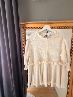 Vit spets top från Zara - Supersöt vit stickad top från Zara med fina spetsdetaljer och volang nedtill. Top har långärmade ärmar och en lös passform, perfekt för en söt look. Mjukt material och vackert mönster upptill.