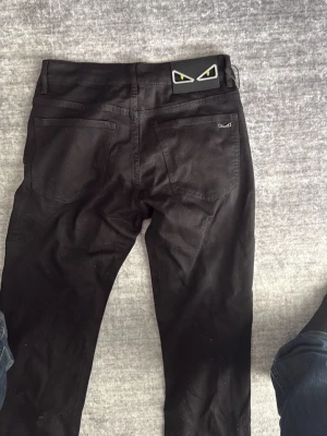 Svarta Fendi Monster jeans - Svarta jeans från Fendi med ikoniska Monster-ögon på bakfickan och patch vid linningen. Slim fit-modell med klassiska fem fickor och snygga detaljer i metall. Perfekta för dig som vill sticka ut med en cool designerlook. HELT SVART. Strechigt material så dem är sköna på!