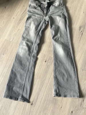 Grå bootcut jeans från Kappahl - Snygga grå jeans från Kappahl i storlek 158. Modellen har bootcut-ben och klassisk femficksdesign. Jeansen har en tvättad look med ljusare partier och är tillverkade i mjukt denimtyg. Perfekta för en avslappnad och trendig stil.