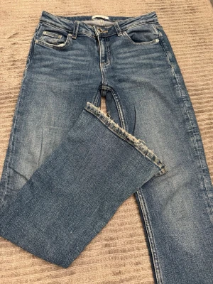Blå jeans med rå kant från Gina Tricot - Snygga blå jeans från Gina Tricot med klassisk femficksmodell och rå, fransad kant nedtill. Jeansen har normal midja och raka ben. Perfekta för en avslappnad och trendig look. Tillverkade i bomull med lite stretch för extra komfort.