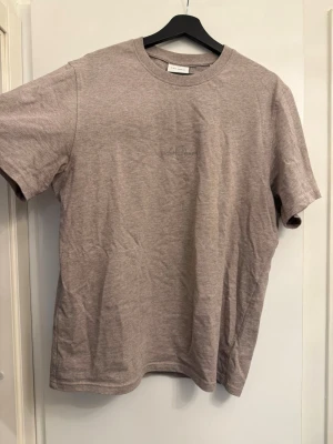 Beige t-shirt från Les Deux - Säljer en stilren beige t-shirt från Les Deux i mjuk bomull. T-shirten har klassisk passform, rund halsringning och diskret broderad logga på bröstet. Perfekt basplagg för en clean och enkel look.