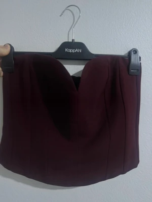 Vinröd korsett-topp med dragkedja helt ny - Vinröd korsett-topp från Zara med markerad sweetheart-urringning och dragkedja bak. Toppen är axelbandslös och har en figurnära passform, perfekt för att skapa en snygg siluett. Materialet känns stadigt och ger bra stöd. Passar både s och m