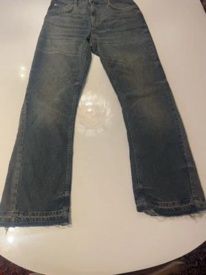Blå flare jeans från Zara - Säljer ett par klassiska blå jeans från Zara med rak passform och råa, fransiga benslut. Jeansen har fyra fickor och är tillverkade i bomull. Perfekta för en avslappnad och trendig look. 
