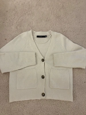 Vit kofta från Vero Moda - Mysig vit kofta från Vero Moda med tre knappar framtill och två stora fickor. Koftan har lång ärm, ribbade muddar och en avslappnad passform. Perfekt att slänga på sig när det är lite kyligt ute. Vill bli av med fort så pris kan diskuteras vi snabb affär! 
