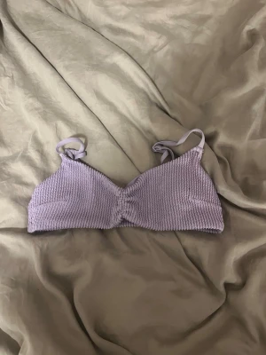 Ljuslila fin bikin top - Säljer en ljuslila bikin top med ribbad struktur och smala axelband. Modellen är utan bygel och har en lätt rynkning framtill. Mjuk och stretchig, perfekt för en avslappnad look. Perfekt nu till sommaren