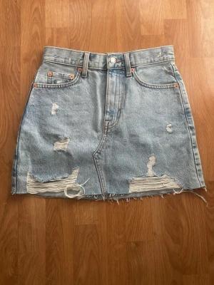 Ljusblå jeanskjol från mango  - Ljusblå jeanskjol i kort modell med rå kant och slitna detaljer framtill.  Kjolen är i väldigt bra skick då den inte har några defekter eller liknande. Kjolen sitter väldigt högt upp på mig men jag är 158 cm dock och drog upp den längre än va den egentligen ska sitta. Så är den hyfsat lång på mig ifall jag dra ner den. Passar perfekt någon som är längre än mig skulle kunna tänka mig.