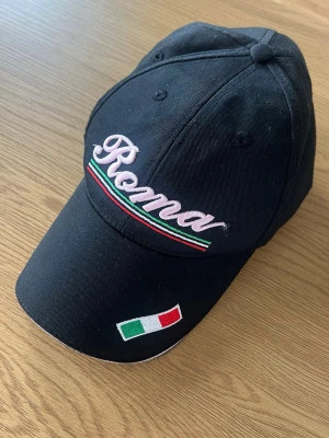 Keps - Snygg svart keps med broderad text 'Roma' i rosa och italienska flaggans färger på skärmen. Kepsen har även en liten italiensk flagga broderad framtill. Justerbar baktill 💕