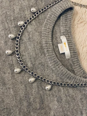 Kedjehalsband med droppformade pärlor - Snyggt halsband med en silverfärgad rostfritt kedja och droppformade vita pärlor som hänger längs hela kedjan. Perfekt för att ge din outfit en cool och trendig touch. Passar till många olika stilar och är lätt att matcha med andra accessoarer.