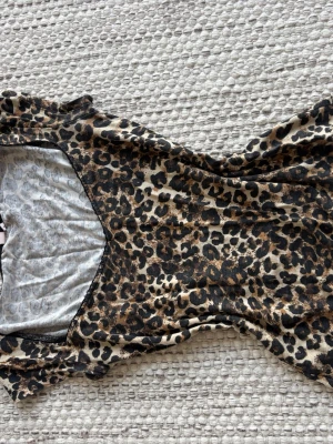 Leopardmönstrad topp i stretchtyg - Säljer en snygg topp med leopardmönster i beige, brunt och svart. Tyget är mjukt och stretchigt, vilket gör den bekväm att bära. Rund halsringning med liten spets och åtsittande passform.