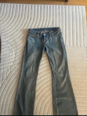 Blå bootcut jeans med klassisk tvätt - Säljer ett par klassiska blå bootcut jeans i denim med fem fickor och kopparfärgade nitar. Jeansen har normal midja och dragkedja med knapp framtill. Perfekta för dig som gillar en avslappnad men ändå snygg stil.