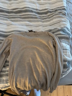 Beige tröja från Oscar Jacobson - Snygg beige tröja från Oscar Jacobson i klassisk modell med rund halsringning och långa ärmar. Perfekt för en stilren och enkel look. Tröjan är tillverkad i ett mjukt material som känns skönt mot huden.