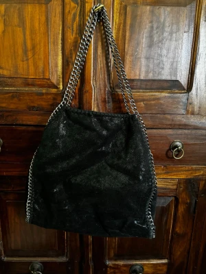 Svart axelväska med kedjedetaljer - Svart väska som liknar Stella Mccartney. Det finns 4 fack totalt - ett stort, två små på sidan och ett litet med dragkedja på andra sidan, så den är rymlig. Använd flitigt men är i gott skick.🫶🏼