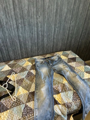 Ljusblå jeans med slitningar - Snygga ljusblå jeans från Replay med klassisk femficksmodell och coola slitningar. Jeansen har raka ben, tydliga sömmar och detaljerade bakfickor med mönster. Perfekta för en avslappnad och trendig stil.