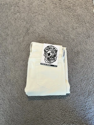 Vita bootcut jeans från Cheap Monday - Säljer ett par vita bootcut jeans från Cheap Monday med klassisk femficksdesign och logga bak på linningen. Jeansen har utsvängda ben och är tillverkade i ett stretchigt denimtyg som sitter snyggt på kroppen.