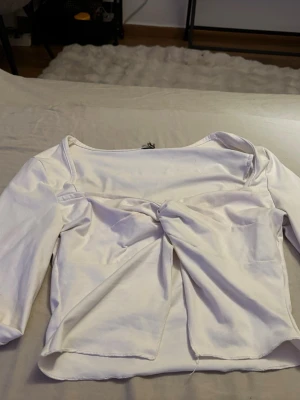 Vit topp med knut framtill - Snygg vit topp med trekvartsärmar och knutdetalj framtill. Toppen har en rak passform och bred urringning, perfekt att styla med jeans eller kjol. Materialet känns mjukt och stretchigt. Säljer denna för den kommer inte till användning den kan ha några fläckar men de inget som märks