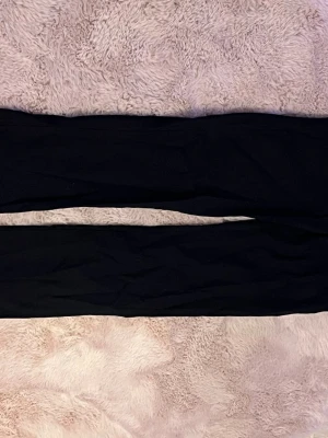 Svarta smala byxor i stretchtyg - Snygga svarta byxor med smal passform och stretchigt material som sitter tajt längs benen men lite luftigare under knäna. Perfekta för dig som gillar en stilren och enkel look. Byxorna har en klassisk design utan synliga detaljer eller mönster.