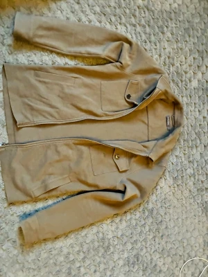 Overshirt från dressman - Stilren beige jacka från dressman med dragkedja framtill och två bröstfickor med lock och knapp. Jackan har en rak passform och är tillverkad i mjukt bomullsmaterial. Perfekt för lager-på-lager och enkel att matcha med olika outfits.