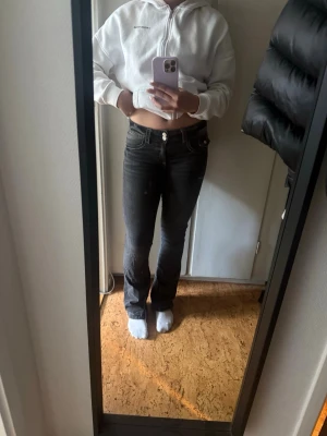 Svarta bootcut jeans med stretch - Snygga svarta bootcut jeans med klassisk femficksdesign och stretchigt material som sitter tajt över låren och släpper ut vid vaden. Jeansen har normal midja och silverfärgade detaljer vid knappar och nitar.