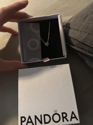 Pandora halsband med hjärthänge - Helt nytt oanvänt halsband från pandora. Sött halsband från Pandora med ett hjärtformat hänge i rosa. Kedjan är i silverfärg och halsbandet levereras i originalask. Perfekt accessoar för att lyfta din stil.