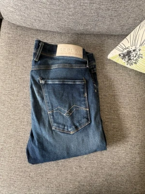 Blå jeans från Replay Anbass - Snygga blå jeans från Replay, modell Anbass. Klassisk femficksdesign med ljusa kontrastsömmar och läderpatch med logga bak i midjan. Jeansen har en smal passform och är tillverkade i stretchigt denimtyg för extra komfort.