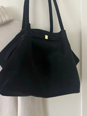 Svart axelväska i mocka-look - Stilren svart axelväska med mjuk mocka-liknande yta och dubbla axelband. Väskan har en enkel design med en liten gulddetalj upptill. Perfekt för dig som vill ha en rymlig och trendig väska till vardagen. Från shein, pris kan diskuteras 🩷aldrig använd