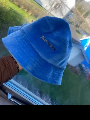 Blå velour bucket hat Juicy Couture - Snygg blå bucket hat från Juicy Couture i mjuk velour. Klassisk form med bred brätte och broderad logga framtill. Perfekt accessoar för att lyfta din streetwear-look.