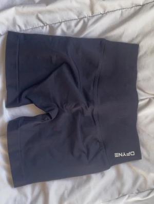 Svarta IMPACT shorts  DFYNE - Svarta seamless shorts från DFYNE med hög midja och tight passform. Perfekta för träning eller chill dagar. Mjukt och stretchigt material som sitter skönt på kroppen. Diskret logga framtill i vitt.