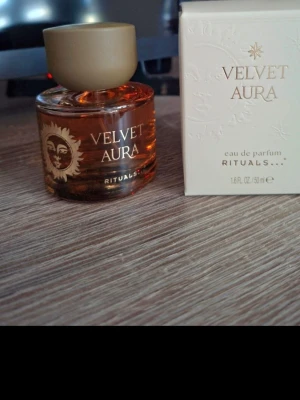 Velvet Aura parfym från Rituals - Velvet Aura eau de parfum från Rituals i en rund glasflaska med guldigt lock och solmotiv. Flaskan är transparent med en varm bärnstensfärgad vätska. Medföljer elegant vit kartong med guldtext. Volym: 50 ml.