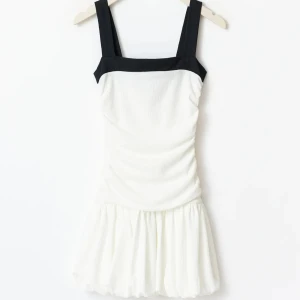Vit kortklänning med svarta axelband - Säljer denna slutsålda supersöta vit kortklänning med breda svarta axelband och fyrkantig ringning. Klänningen har en figurnära överdel och en fluffig, volangig kjol som ger en lekfull vibe. Perfekt för dig som vill sticka ut med en stilren men ändå unik look. Klänningen är helt ny med prislapp. Storlek M men passar S också. Det är 14+